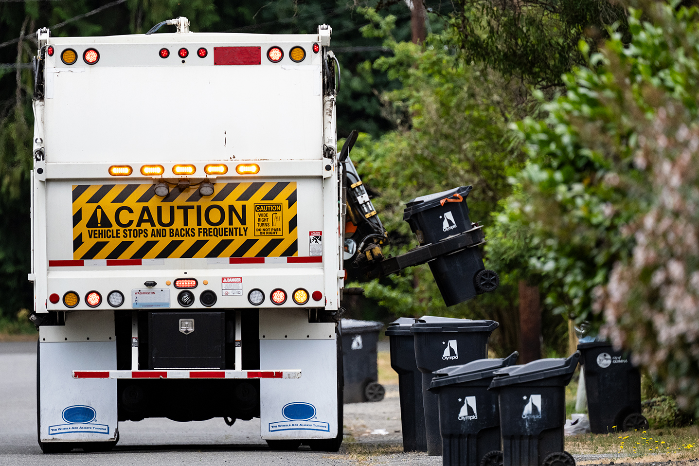 A garbage collection truck picks up and empties a line of residential trash bins.